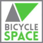 A square logo with a gray triangle and a green triangle above the words “BICYCLE SPACE,” with “BICYCLE” in gray and “SPACE” in green, all on a white background with a gray border.